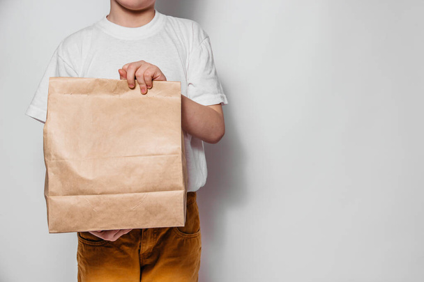 Brown craft paper bag for the removal or delivery of goods and food in hands on a white background. Place for advertising and copy space. delivery service concept - Φωτογραφία, εικόνα