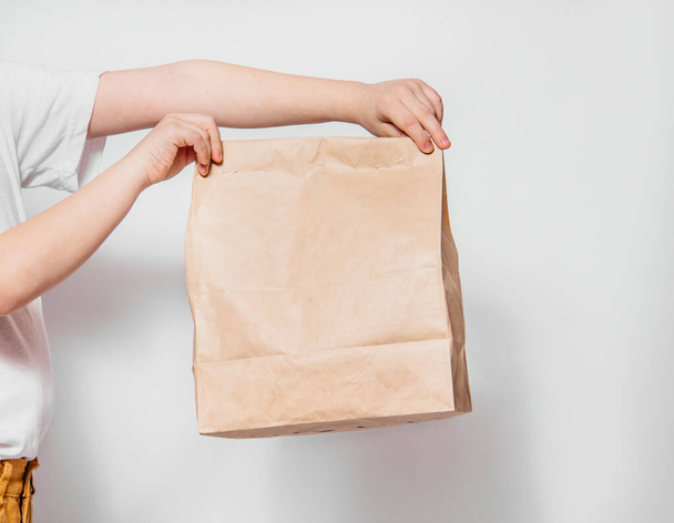 Brown craft paper bag for the removal or delivery of goods and food in hands on a white background. Place for advertising and copy space. delivery service concept - Фото, изображение