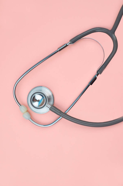 One single normal stethoscope isolated on top of a pink color empty paper background - Foto, Bild
