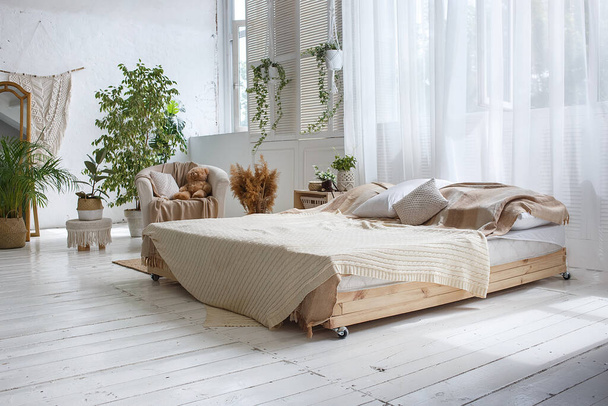 Elegante luminoso loft acogedora habitación con cama doble, sillón, plantas verdes, cortinas, paredes de ladrillo blanco y suelo de madera
. - Foto, imagen