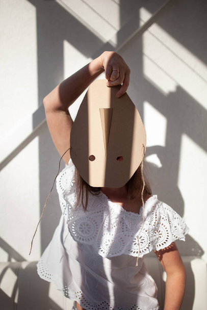 Portrait of a woman. A female hides his face behind a cardboard mask, indoor - Photo, image