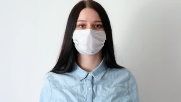 closeup of a young smiling woman, a girl with long brown hair takes off a medical protective mask, sighs heavily, looks at the camera, concept of hygiene covid-19, coronavirus, on a white background - Záběry, video