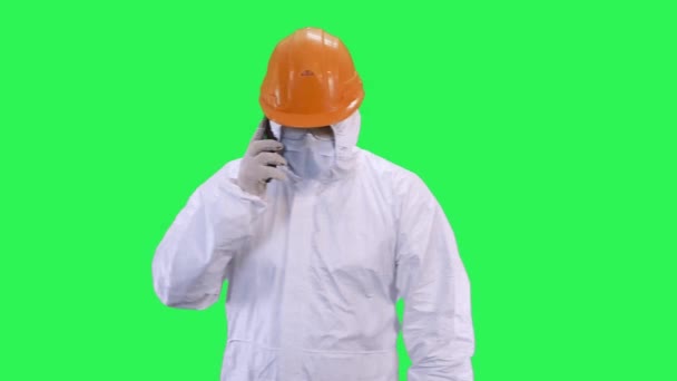 A man in a helmet and a protective suit is talking on the phone in high tones.Green screen background. - Кадри, відео