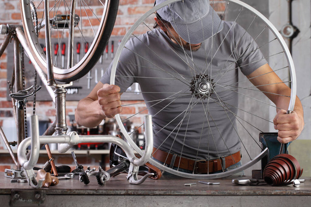 man repareert de vintage fiets in garage werkplaats op de werkbank met gereedschap, diy concept - Foto, afbeelding