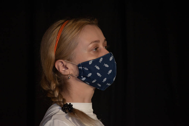 Жінка в захисній масці. Молода жінка вдома зробила гігієнічну маску для обличчя, щоб запобігти зараженню, хворобі або грипу та 2019-nCoV. Чорний фон. Захист від хвороб, коронавірус
. - Фото, зображення