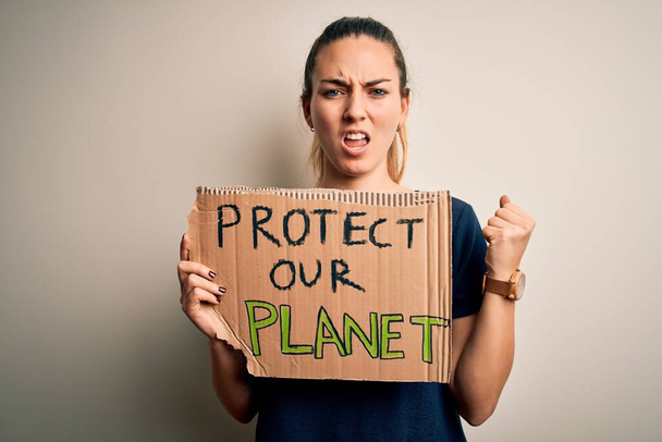 Young beautiful blonde woman with blue eyes asking for protect planet holding banner annoyed and frustrated shouting with anger, crazy and yelling with raised hand, anger concept - Photo, Image