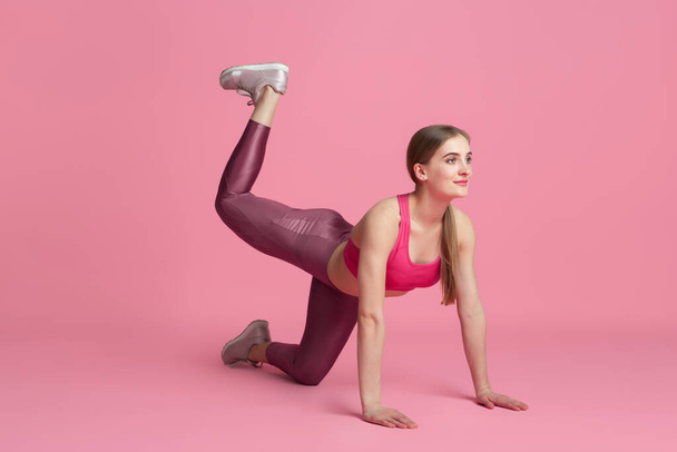 Beautiful young female athlete practicing on pink studio background, monochrome portrait - Фото, изображение