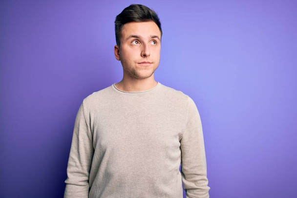 Young handsome caucasian man wearing casual sweater over purple isolated background smiling looking to the side and staring away thinking. - Photo, Image