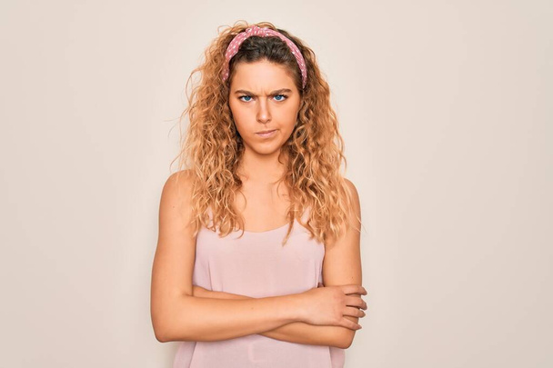 Νεαρή όμορφη γυναίκα με μπλε μάτια φορώντας casual t-shirt και diadem πάνω από ροζ φόντο σκεπτικός και νευρικός, αποδοκιμάζοντας έκφραση στο πρόσωπο με σταυρωμένα χέρια. Αρνητικό πρόσωπο. - Φωτογραφία, εικόνα