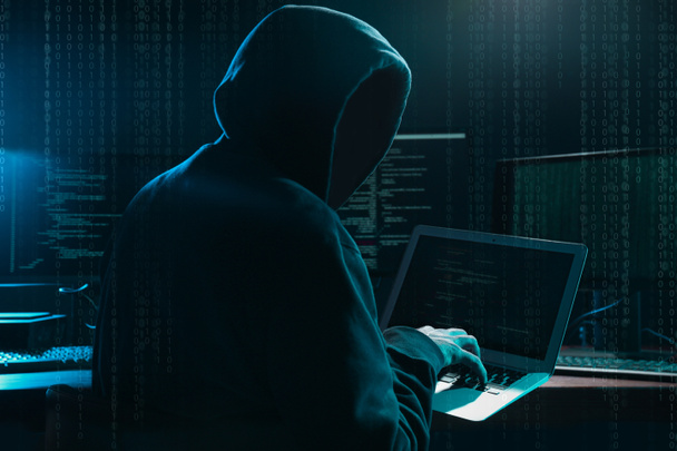Кібер-злочинець зламує систему за столом, цифровий двійковий код на передньому плані. - Фото, зображення