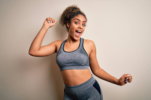 Young african american sportswoman doing sport wearing sportswear over white background Dancing happy and cheerful, smiling moving casual and confident listening to music - Foto, Imagen