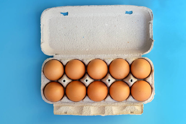 Cardboard tray for ten eggs top view. Brown chicken eggs in a paper box on a blue background. Eggs in a paper container. - Zdjęcie, obraz