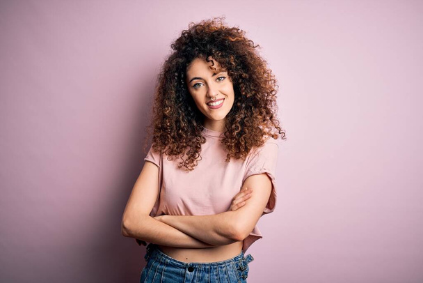 Young beautiful woman with curly hair and piercing wearing casual pink t-shirt happy face smiling with crossed arms looking at the camera. Positive person. - Photo, Image