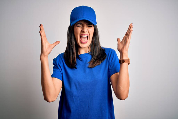 Νεαρή γυναίκα παράδοση με μπλε μάτια φορώντας καπέλο στέκεται πάνω από το μπλε φόντο γιορτάζει τρελός και τρελός για την επιτυχία με τα χέρια υψωμένα και κλειστά μάτια ουρλιάζοντας ενθουσιασμένος. Έννοια νικητή - Φωτογραφία, εικόνα