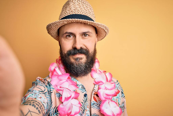Jóképű, kopasz férfi szakállal és tetoválással vakáción, nyári kalapban és hawaii lejben, boldog arccal, állva és mosolyogva, magabiztos mosollyal a fogain. - Fotó, kép