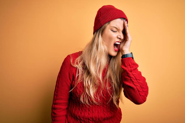 Young beautiful blonde woman wearing casual sweater and wool cap over white background Yawning tired covering half face, eye and mouth with hand. Face hurts in pain. - Photo, Image