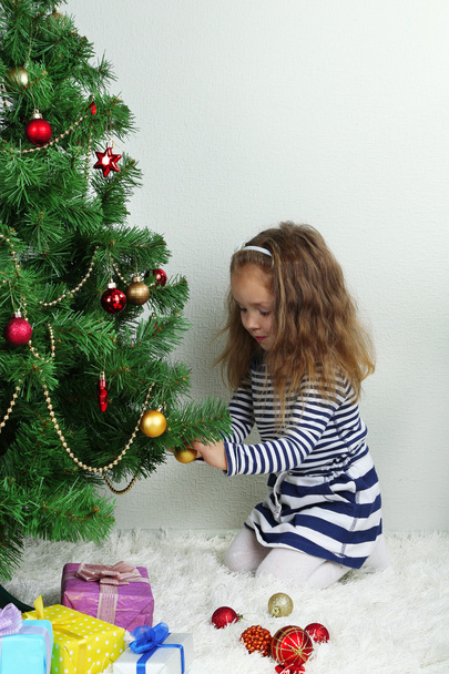 Little girl decorating Christmas tree with baubles in room - 写真・画像