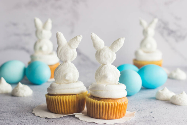 Cute easter composition. Blue easter eggs, meringue easter bunnies and raisin carrot muffins - Фото, зображення