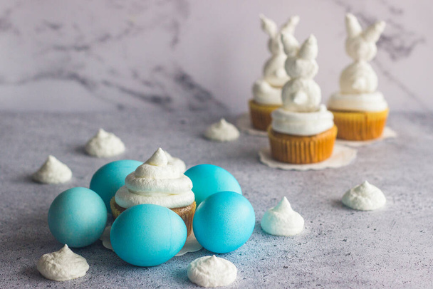 Cute easter composition. Blue easter eggs, meringue easter bunnies and raisin carrot muffins - Φωτογραφία, εικόνα