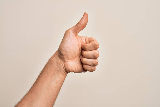 Mão de jovem caucasiano mostrando dedos sobre fundo branco isolado fazendo gesto de aprovação bem sucedida com polegares para cima, validação e símbolo positivo - Foto, Imagem