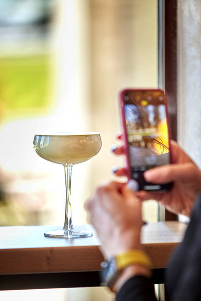 The concept of a blogger photographing alcoholic beverages in a transparent glass. A glass on a thin leg. Blogging about drinks. - Foto, Imagem