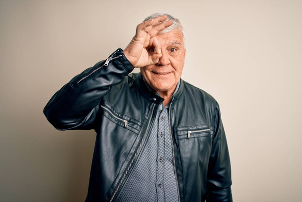Senior handsome hoary man wearing casual shirt and jacket over isolated white background doing ok gesture with hand smiling, eye looking through fingers with happy face. - Foto, afbeelding