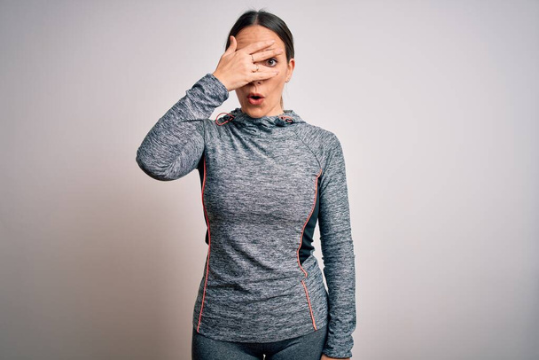 Fiatal szőke fitness nő visel sport edzőruha felett elszigetelt háttér kukucskál a sokk fedő arc és a szem kézzel, nézi az ujjakon keresztül zavarba ejtő kifejezés. - Fotó, kép