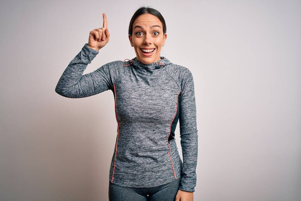 Fiatal szőke fitness nő visel sport edzőruha felett elszigetelt háttér mutatva ujj fel a sikeres ötlet. Kilépett és boldog. Egyes számú.. - Fotó, kép