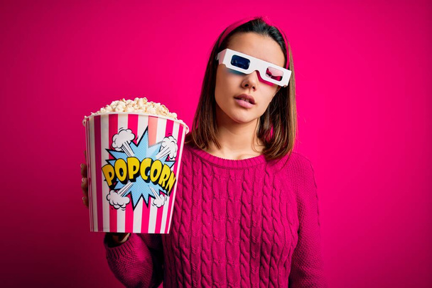 Young beautiful girl watching movie using 3d glasses eating box with popcorns looking sleepy and tired, exhausted for fatigue and hangover, lazy eyes in the morning. - Photo, Image