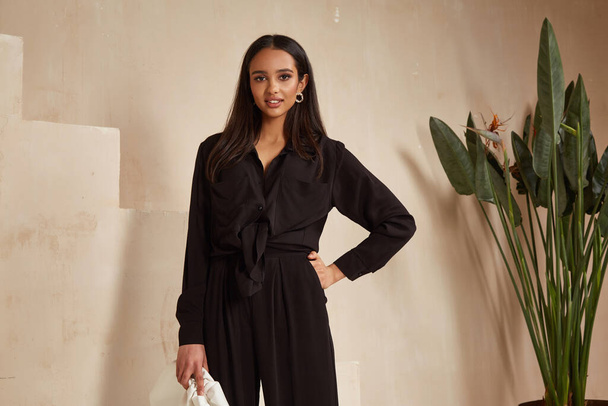 Beautiful brunette woman natural makeup wear fashion clothes casual dress code office style total black blouse and pants suit, romantic date business meeting accessory bag interior stairs flowerpot. - 写真・画像