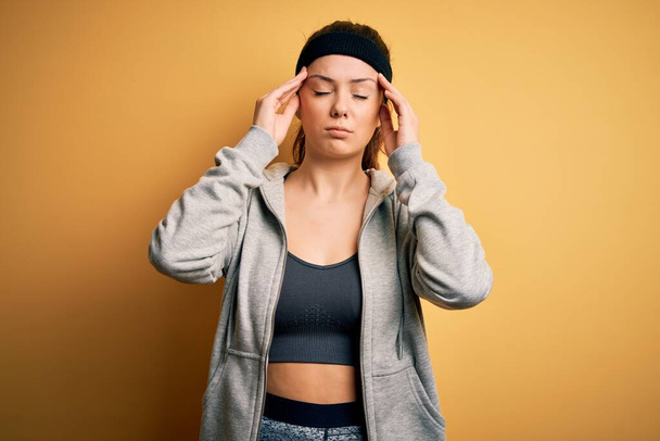Fiatal gyönyörű barna sportos nő visel sportruházat sárga háttér szenved fejfájás kétségbeesett és hangsúlyozta, mert a fájdalom és a migrén. Kezeket a fejre!. - Fotó, kép