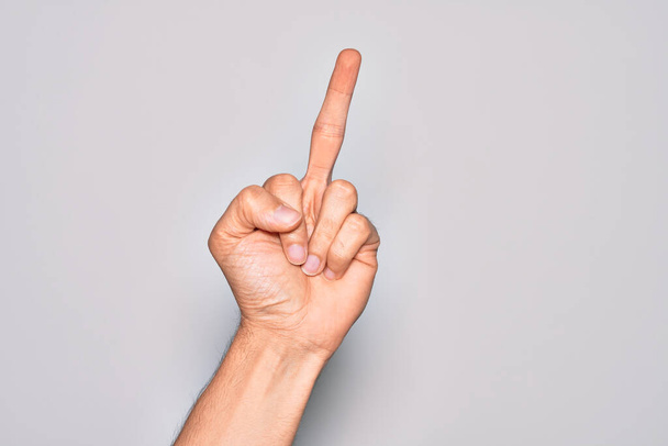 Hand of caucasian young man showing fingers over isolated white background showing provocative and rude gesture doing fuck you symbol with middle finger - Foto, Imagem