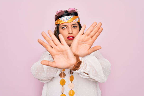 Mujer hippie hispana joven que usa estilo boho de moda y gafas de sol sobre fondo rosa Expresión de rechazo cruzando brazos haciendo signo negativo, cara enojada
 - Foto, Imagen