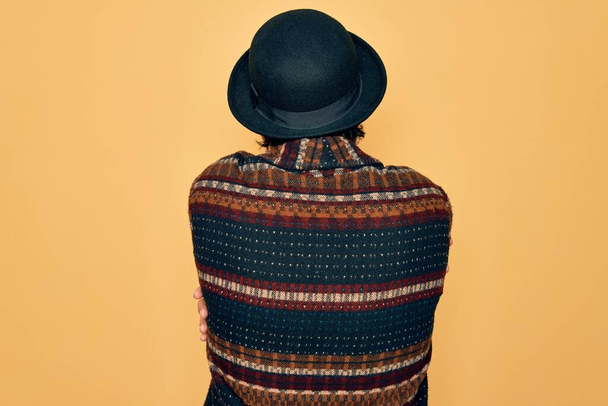 Junger gutaussehender hispanischer Bohemien mit Hippie-Stil und Boho-Hut, der sich von hinten glücklich und positiv umarmt. Selbstliebe und Selbstfürsorge - Foto, Bild