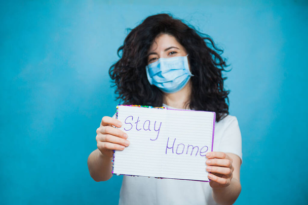 Молодая и красивая женщина в противовирусной маске держит письменный текст остаться дома
. - Фото, изображение