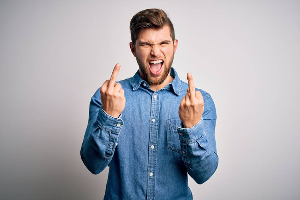 Young handsome blond man with beard and blue eyes wearing casual denim shirt Showing middle finger doing fuck you bad expression, provocation and rude attitude. Screaming excited - Φωτογραφία, εικόνα
