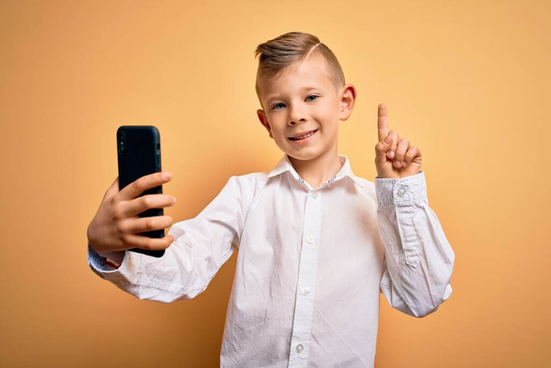 Jovem garoto caucasiano usando smartphone e olhando para a tela do telefone surpreso com uma ideia ou pergunta apontando o dedo com o rosto feliz, número um
 - Foto, Imagem