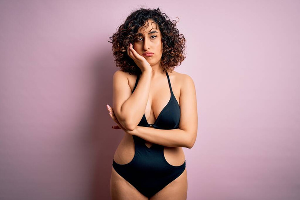 Young beautiful arab woman on vacation wearing swimsuit and sunglasses over pink background thinking looking tired and bored with depression problems with crossed arms. - Foto, Bild