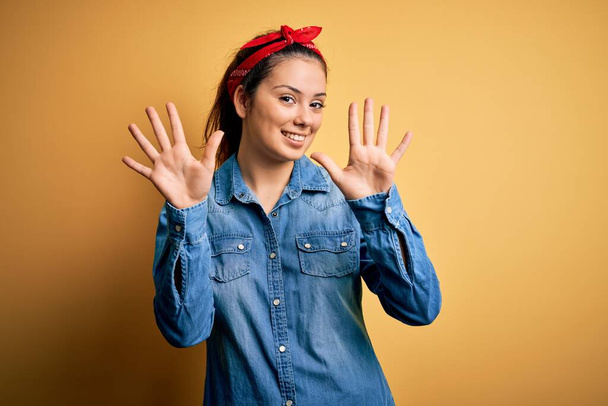Young beautiful brunette woman wearing casual denim shirt and hair handkerchief showing and pointing up with fingers number ten while smiling confident and happy. - Zdjęcie, obraz