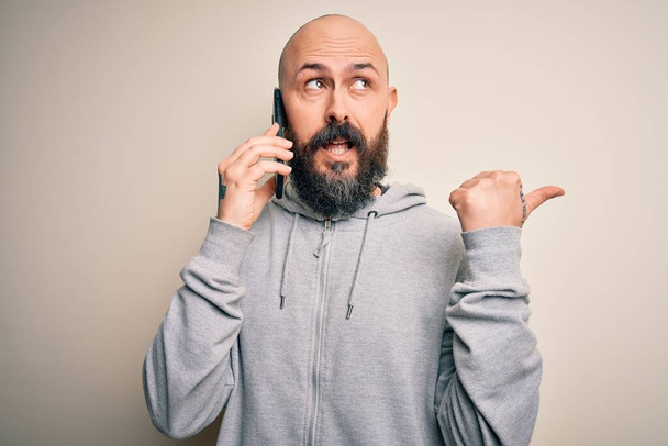 Pohledný plešatý muž s vousy při rozhovoru mluví na smartphonu ukazuje palcem nahoru na stranu se šťastnou tváří usmívá - Fotografie, Obrázek