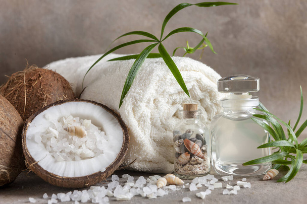 Close-up of Coconut, soft towels, coconut essence, sea salt, shells and tropical greens. Spa concept, beauty and health salon, cosmetics store. - Photo, image