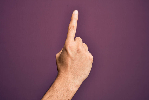 Hand eines kaukasischen jungen Mannes mit Fingern über isoliertem lila Hintergrund, der die Zahl eins mit dem Zeigefinger zählt und dabei Idee und Verständnis zeigt - Foto, Bild