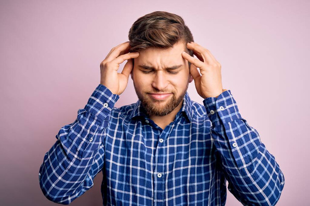 Young handsome blond man with beard and blue eyes wearing casual shirt standing suffering from headache desperate and stressed because pain and migraine. Hands on head. - Photo, Image