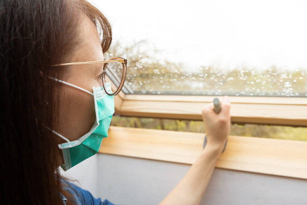 Woman wearing facial medical mask opening window in a sunny day - Photo, image