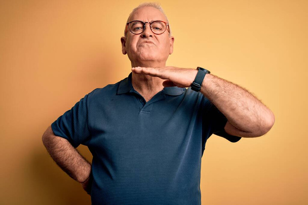 Middle age handsome hoary man wearing casual polo and glasses over yellow background cutting throat with hand as knife, threaten aggression with furious violence - Photo, Image