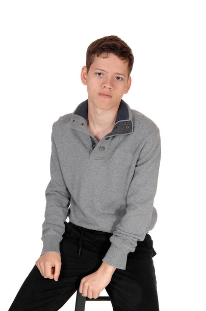 A happy young teenage boy sitting on a chair in the studio in a gra - Φωτογραφία, εικόνα