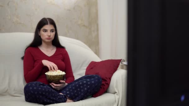Woman relaxing on couch watching TV eating popcorn movie films cozy home evening - Imágenes, Vídeo
