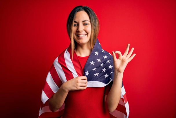 Молода красива блондинка патріотична жінка з блакитними очима в об'єднаних штатах прапор робить знак з пальцями, відмінний символ
 - Фото, зображення