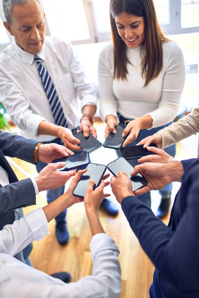 Group of business workers standing with hands together using smartphone doing symbol at the office - Photo, Image