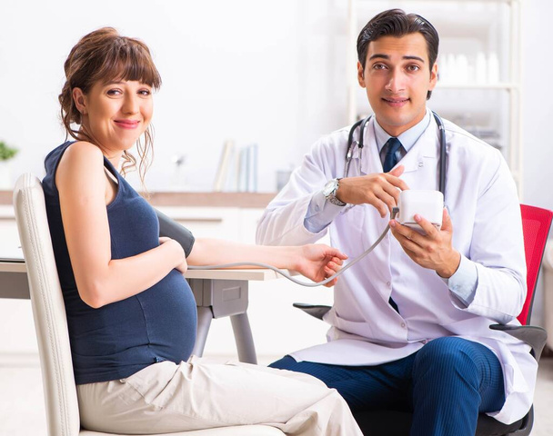 Young doctor checking pregnant womans blood pressure - Foto, Bild
